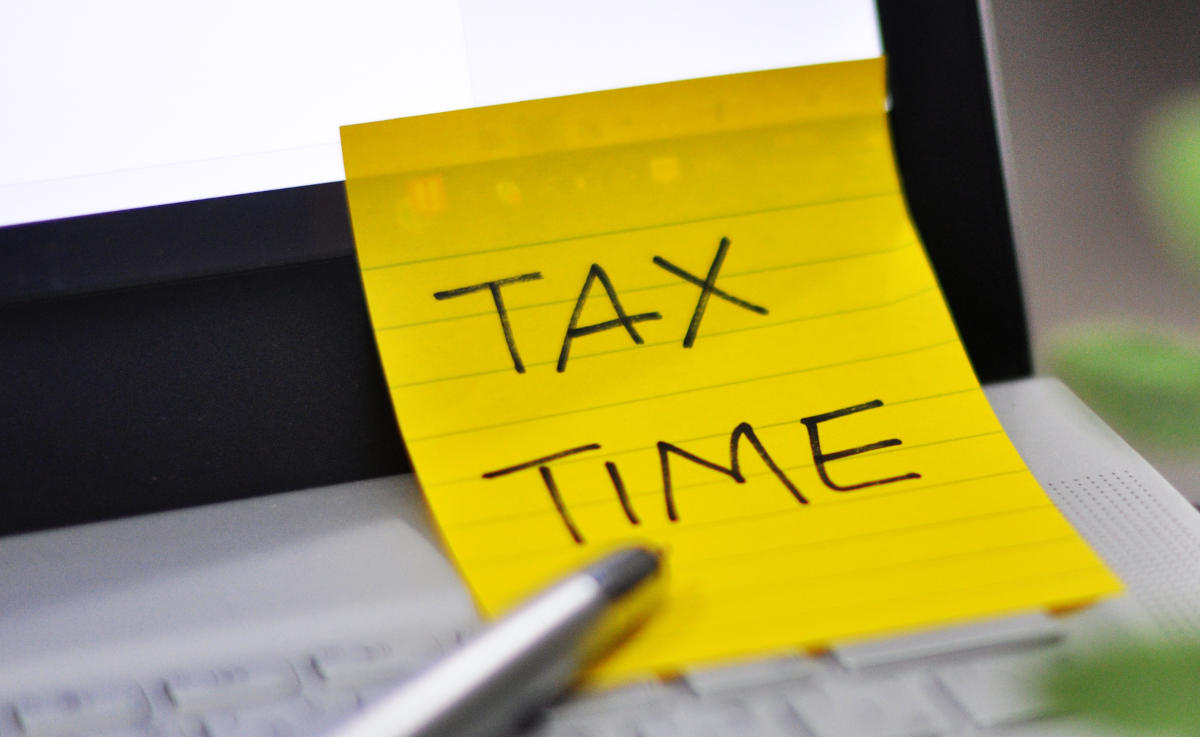 View of an office laptop background with a metallic pen and a Tax Time note pad reminder attached to it