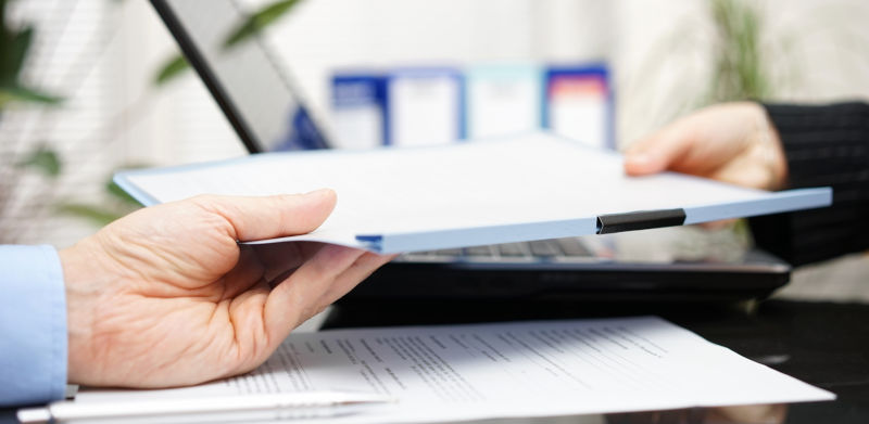 A file moving from one hand to another on top of a pile of documents lying on a table