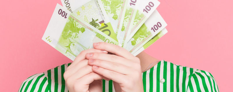 A woman holding bills in front of her face