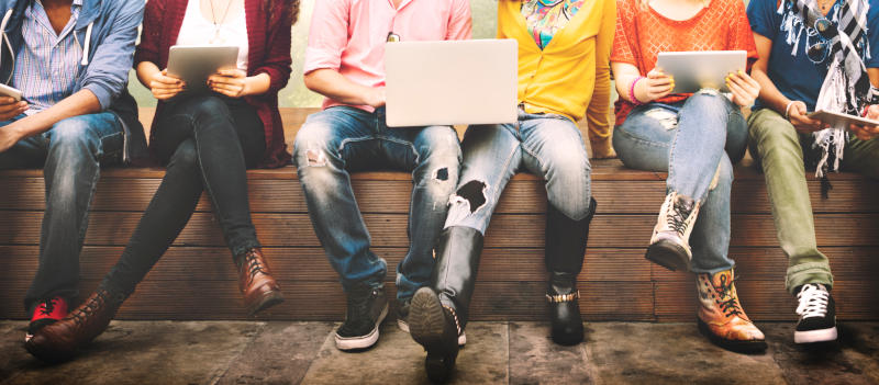 Students sitting on a bench holding tablets and computers